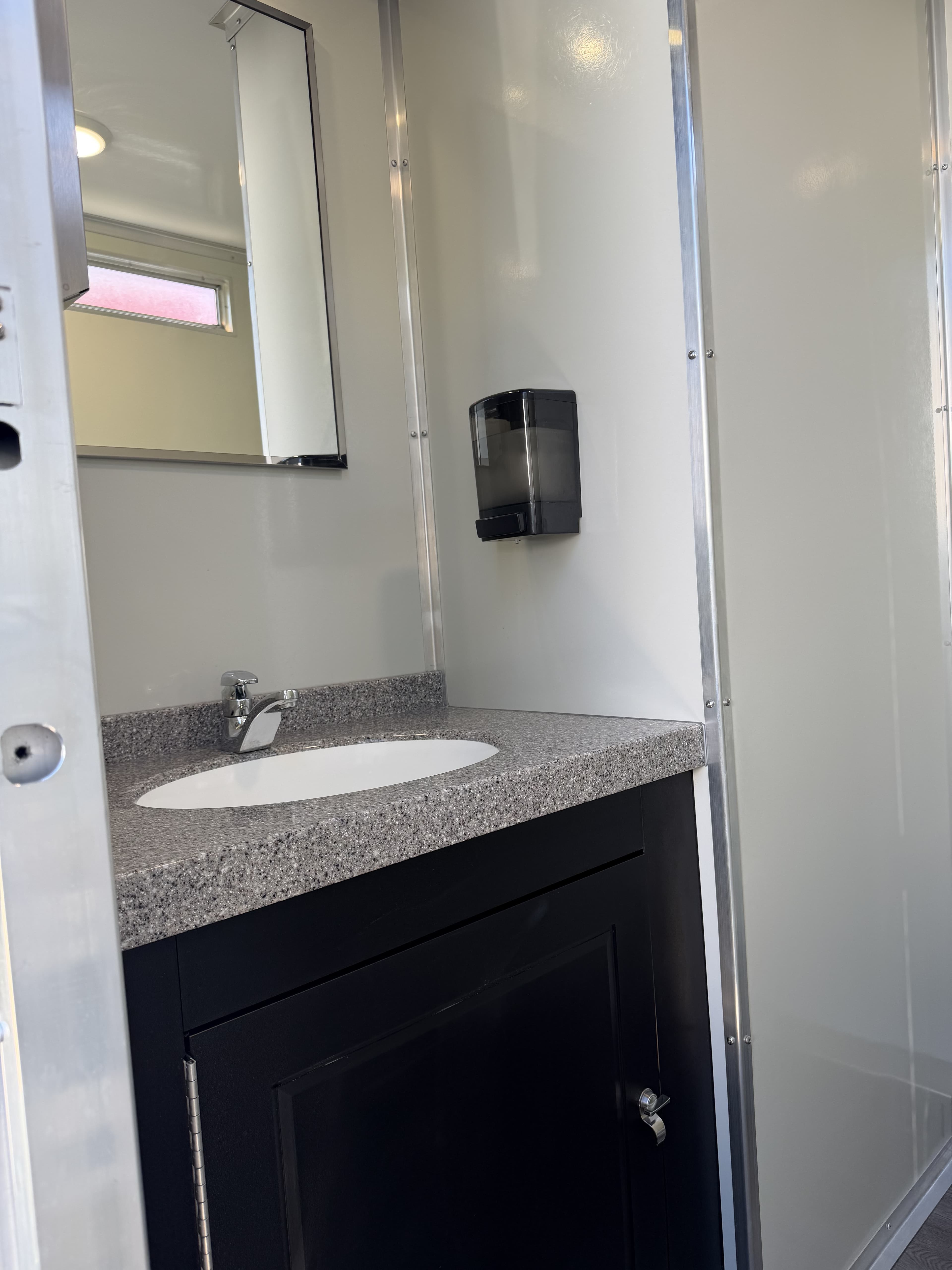 Vanity with a porcelain sink, chrome faucet, granite-look countertop, framed mirror, and soap dispenser